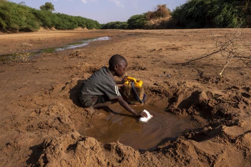 A young boy collects what little water he can from dirty hole dug in a dried up river due to severe drought. Dollow, Somalia.