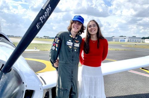 Mack and Ms. Rutherford stand in front of one wing of the microlight planeat the end of Mack's journey. The propeller is visible in the left foreground.