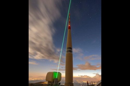 Image of a laser path shooting along the side of the 124-meter-high telecommunication tower of Säntis, Switzerland.