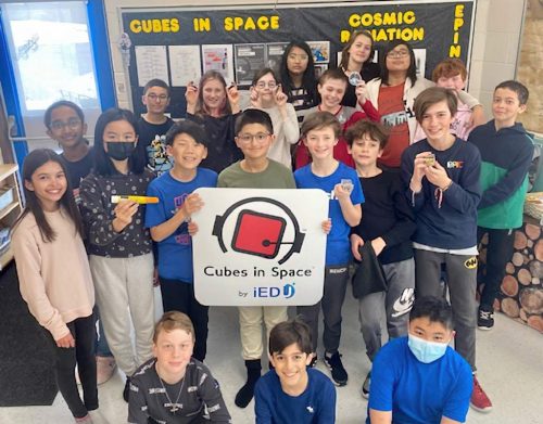 A large group of students holding an EpiPen and two cubes used the experiment, along with a sign saying "Cubes in Space".