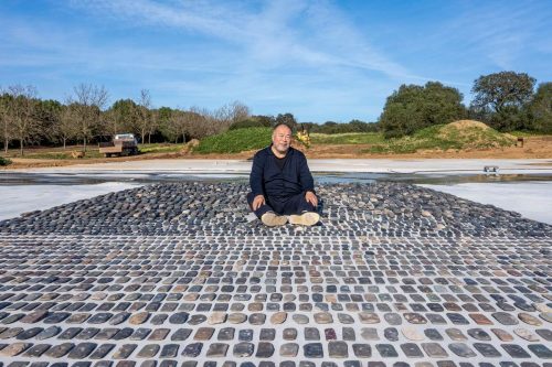 Ai Weiwei, seated in one of his artworks made of hundreds of carefully placed flat stones.