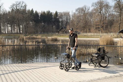 Gert-Jan is shown walking by a lake with the digital bridge. The empty wheelchair sits behind him.