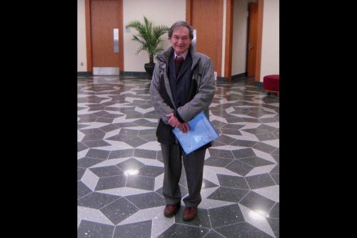 Roger Penrose in the foyer of the Mitchell Institute Building at Texas A&M University, standing on a floor with Penrose tiling.