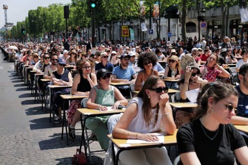Participants sitting at desks on the Champs-Elysees prepare to take part in the Big Dictation.