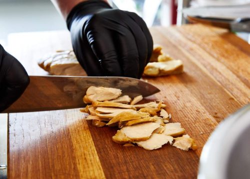 Good Meat chicken being slicked thinly by gloved hands.