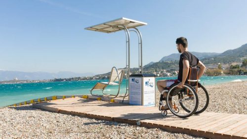 A man wheels his wheelchair along a wooden walkway toward the chair of the Seatrac system.