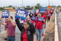 Striking UAW workers march by roadside holding signs.