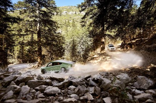 The solar car is seen racing down a dusty, dirty boulder-lined mountain forest road.