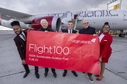 Crew members and leaders of Virgin Atlantic hold a sign saying "Flight 100, 100% Sustainable Aviation Fuel" in front of a Virgin Atlantic 787.
