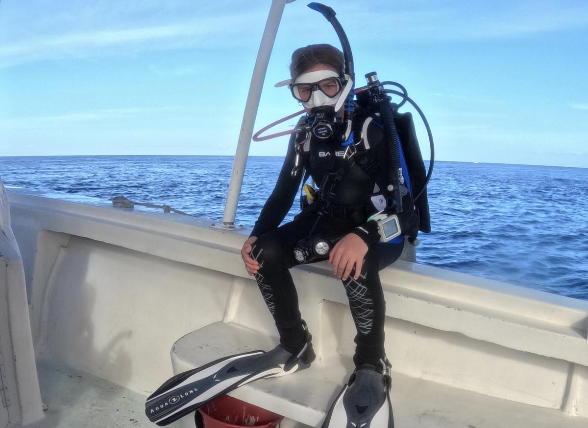 Mia DaPonte seen in mask and full scuba gear, seated on the edge of the boat, ready to drop into the water for a dive.