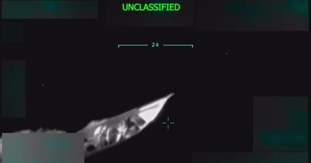 Still image of a boat from a video showing the boat being hit by a US attack, killing 11 people. A grainy black and white image with the word "UNCLASSIFIED" printed in green at the top. The image appears to be taken through a viewfinder and is mainly black, but shows a white speedboat near the center. A crosshairs icon appears near the boat.