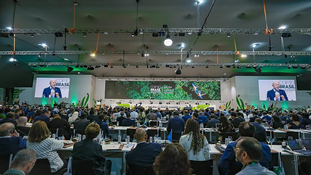Luiz Inácio Lula da Silva speaks during the opening session of the COP30 meeting in Belém, Brazil. He appears on two large screens on either side of the image. In the foreground are hundreds of representatives listening to the speech.