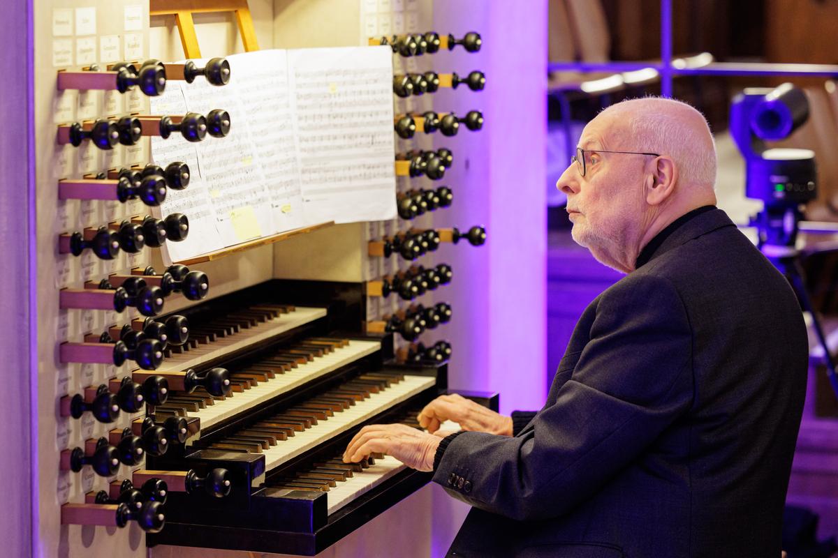 Ton Koopman is shown playing the two chaconnes written by Johann Sebastian Bach. An older man is seen seated at an organ with four keyboards arranged like stairs in front of him. Above the keyboards is the music.