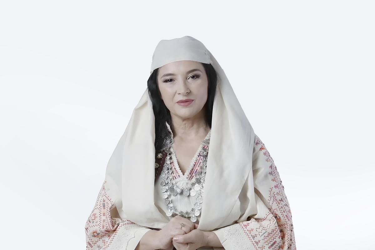 Albania's AI-generated minister "Diella" Wearing a flowing white headscarf and a traditional decorative gown, a Brown-haired woman with clasped hands looks directly at the camera lens. The background behind her has been removed and filled with white.
