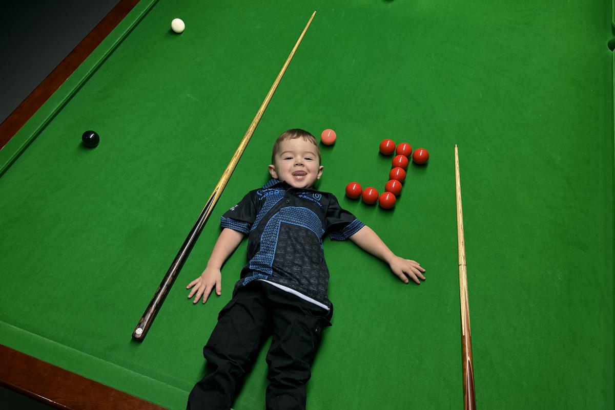 Jude Owens lies back on a snooker table, with a cue on either side of him, and red balls forming the letter J.