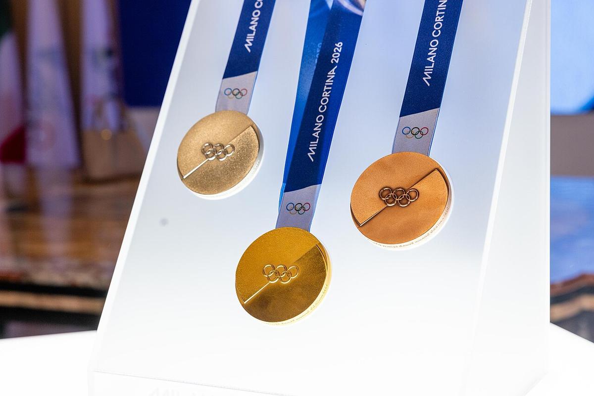Medals of 2026 Winter Olympics. Three Olympic medals made of different metals hang by their straps on a white display easel. The straps read Milano Cortina 2026.