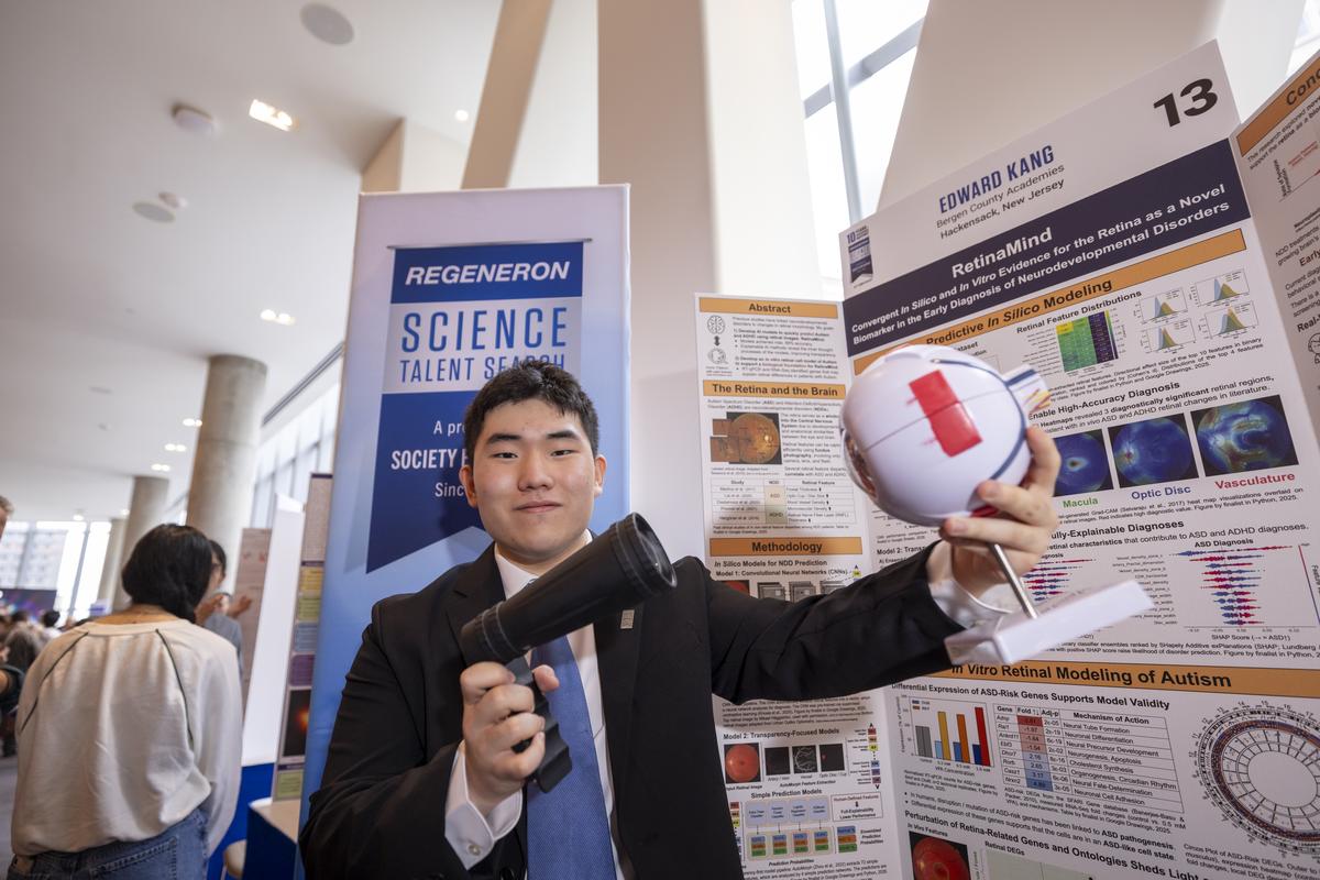 Edward Kang poses with his second place project, RetinaMind. He's holding a model of the human eye and a device that appears to be scanning it.