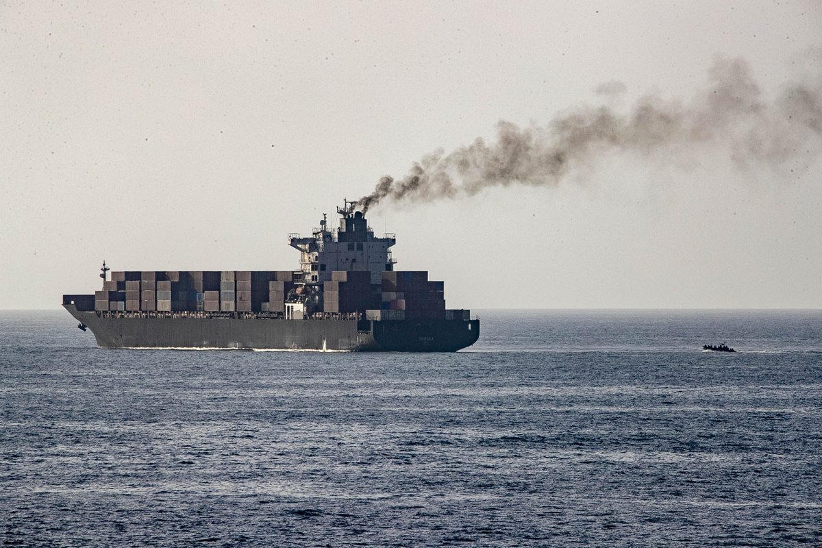 A small boat is seen speeding toward a smoking cargo ship.
