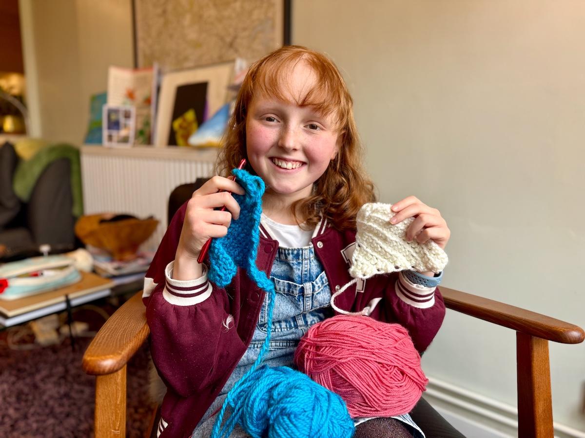 Kirsty smiles as she holds up two crocheted triangles meant to be used as bunting.