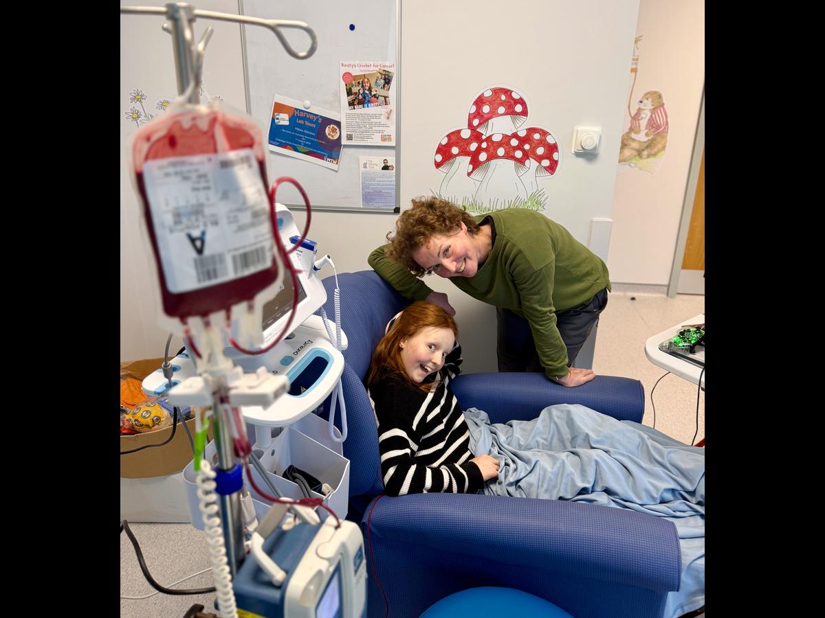 A picture of Kirsty and her mom as Kirsty is getting a blood transfusion. Kirsty is mugging for the camera and her mom is smiling.