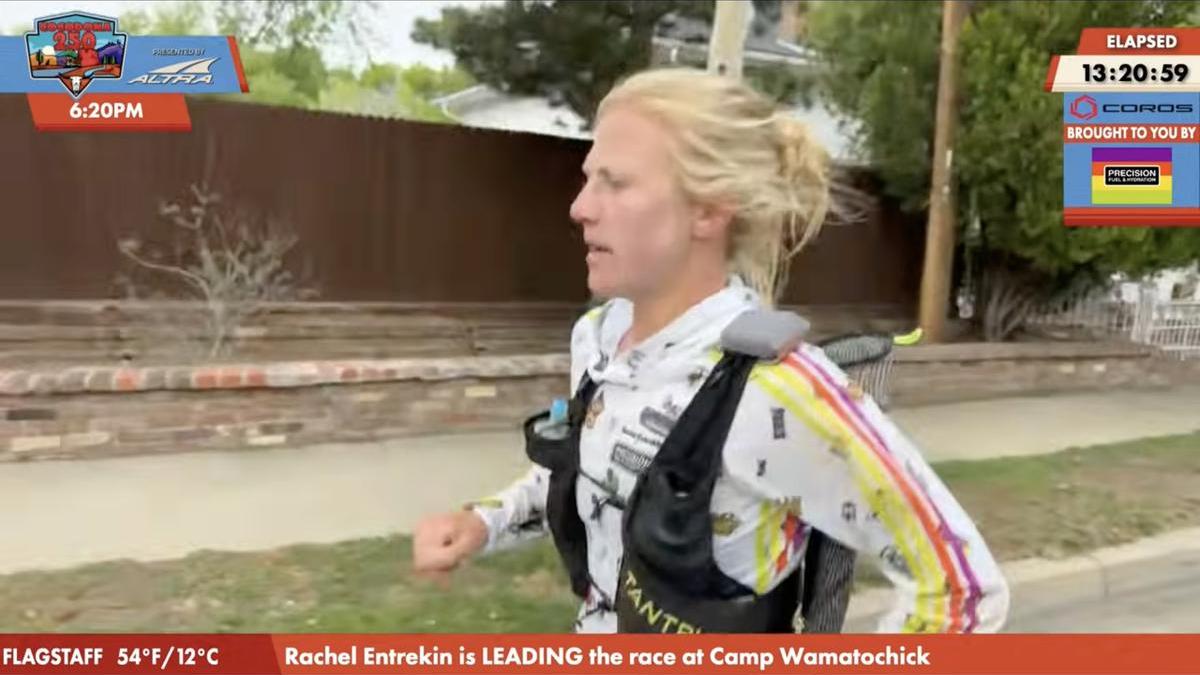 US athlete Rachel Entrekin makes history as first woman to win Cocodona 250 ultramarathon. Waist up shot of a blonde woman wearing a running vest running along a street with a brown fence in the background.