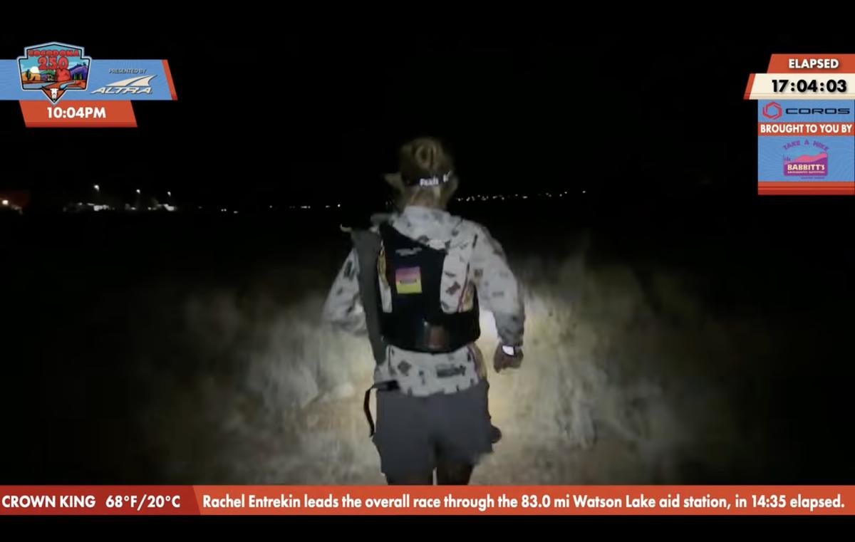 US athlete Rachel Entrekin makes history as first woman to win Cocodona 250 ultramarathon. Entrain is seen from behind as she runs through a field at night. The field ahead of her is lit by her headlamp.