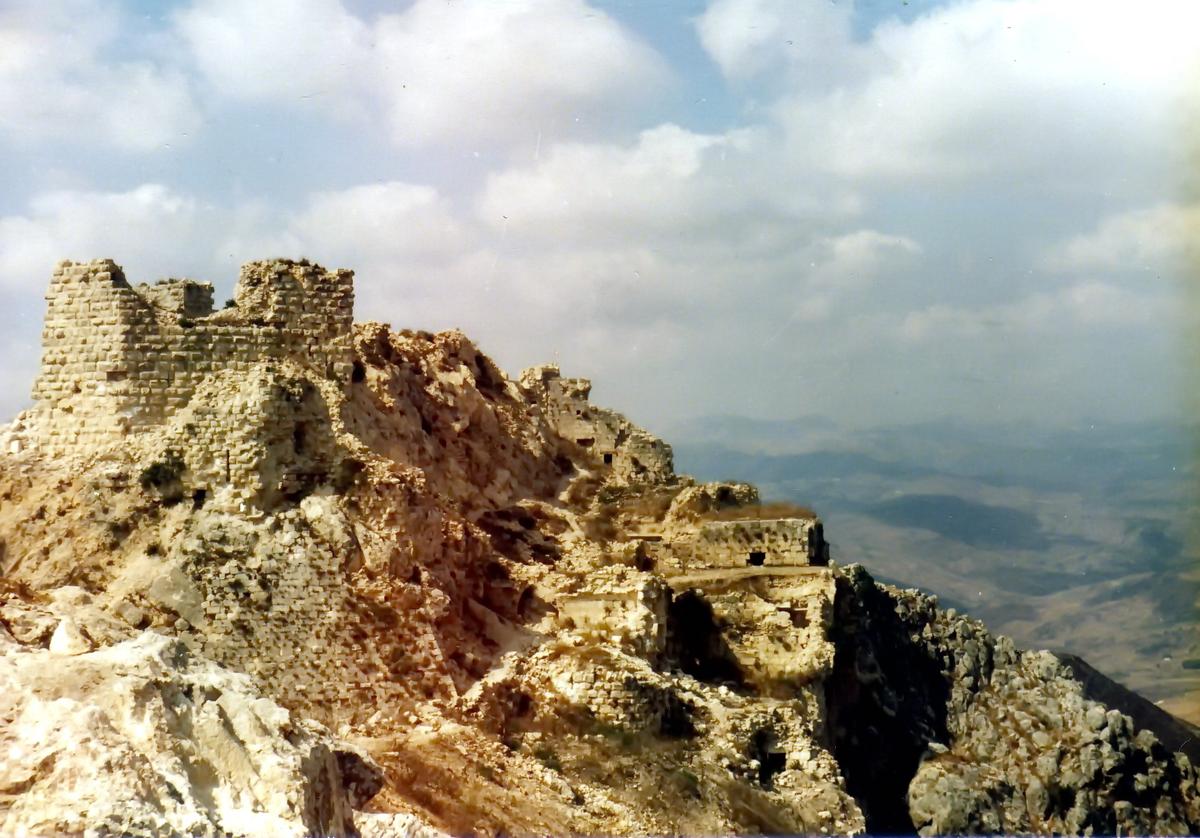 Beaufort Castle, South Lebanon, 1982. An ancient stone castle on a rocky hilltop in an arid landscape is seen against a backdrop of clouds in the sky.
