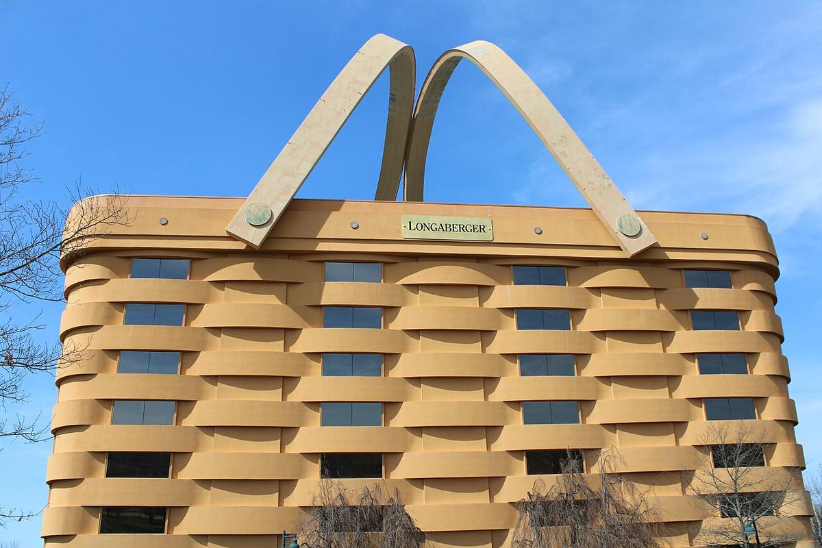 The unoccupied headquarters of The Longaberger Company, also known as the basket building seen from the front entrance. A large, multi-story tan building designed to resemble a woven wicker basket with two handles leaning over its roof.