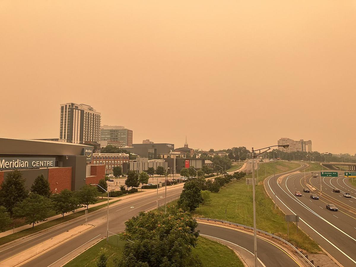 Wildfire smoke in St. Catharines, Ontario and Niagara Region. Smoke originated from the 2026 wildfires in the prairies. City buildings are seen to the left, and a highway is seen to the right. The sky over both is a bruised, dirty orange.